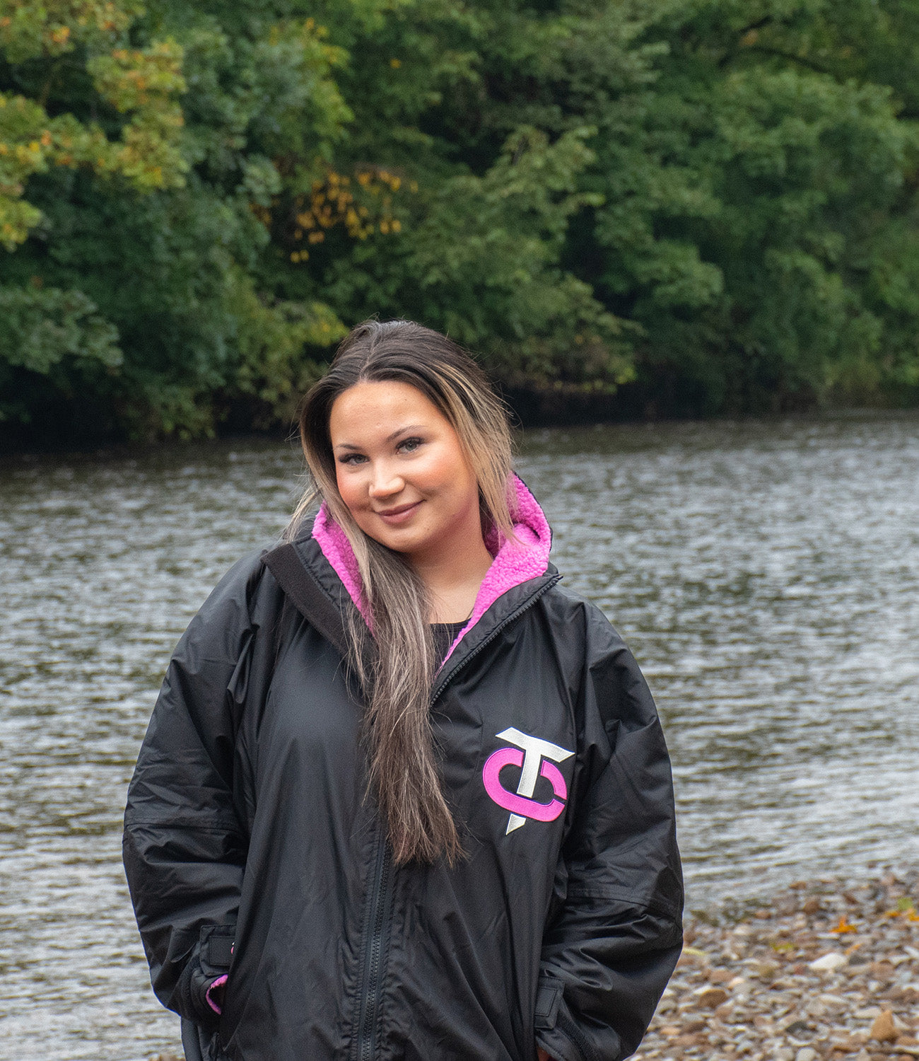 Image of a woman wearing a black and pink T-Robe infront of a river