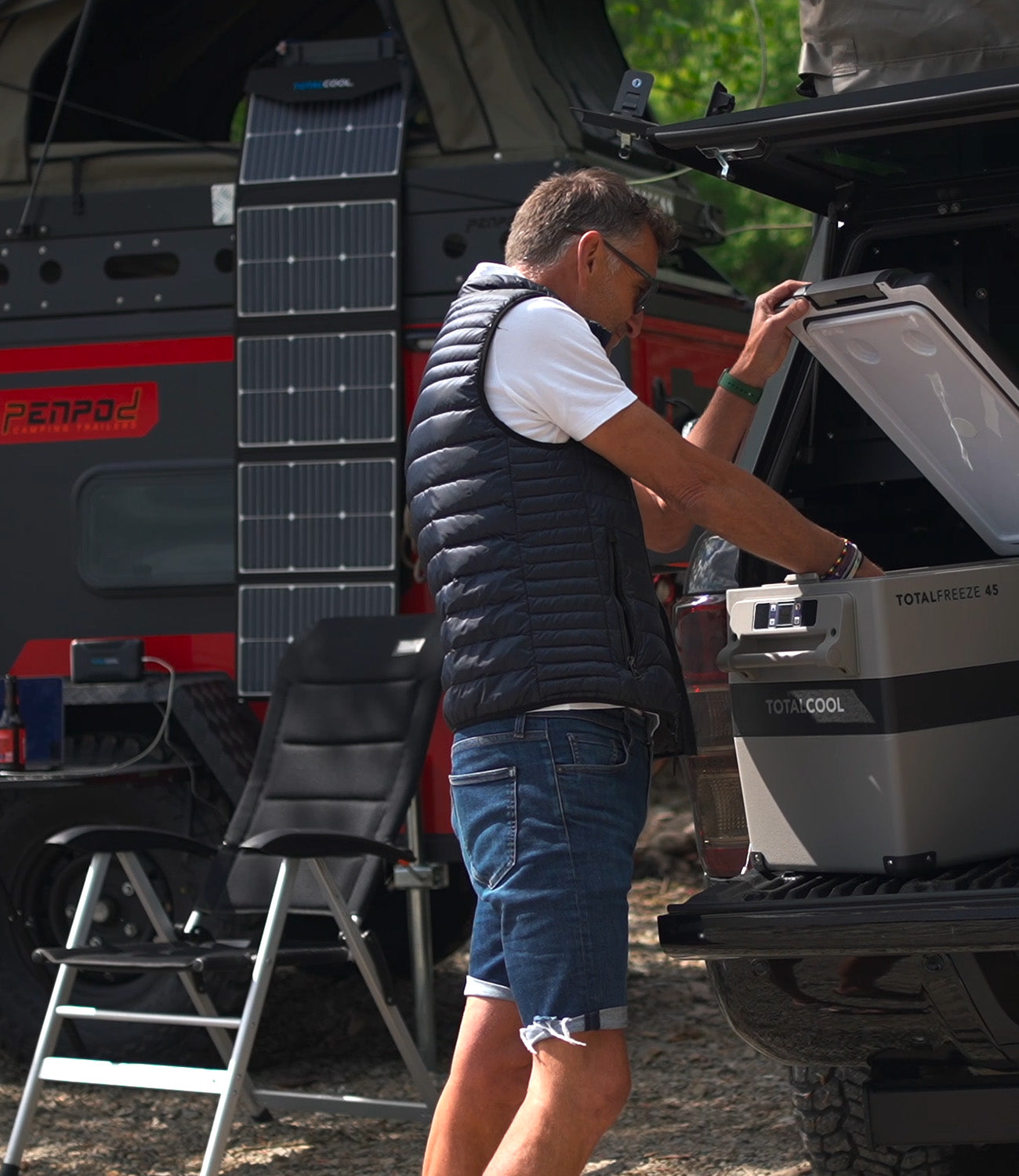 Image of a man outside of his motorhome that has TS100 Solar panels hanging off the side whilst rummaging in a Totalfreeze 45 Fridge freezer in the boot of his car