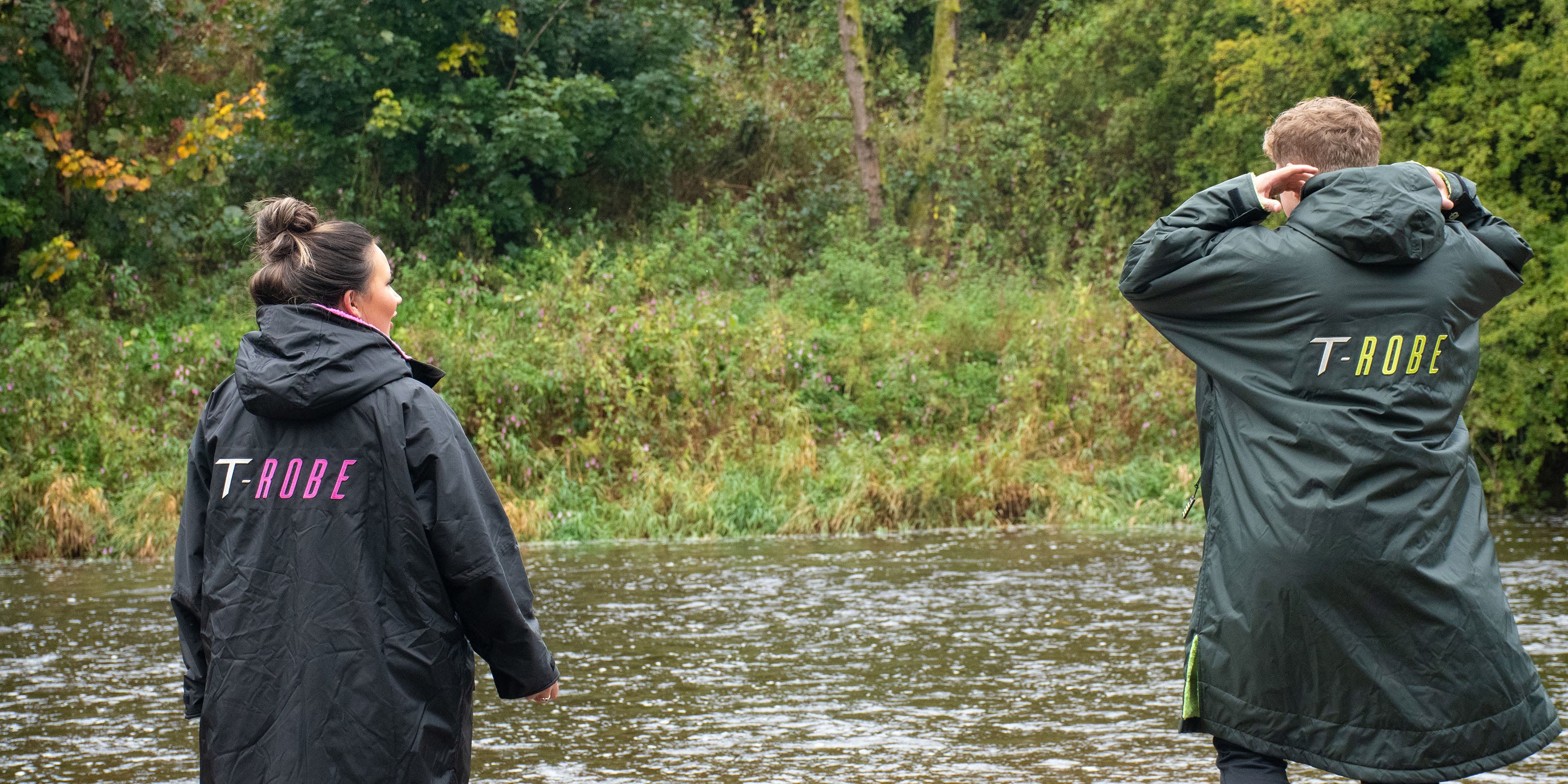 Image of a man and woman wearing changing ponchos next to a river