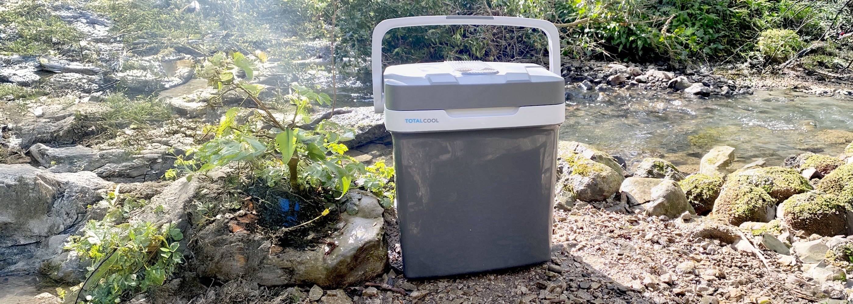 Image of the Eco-chill 24 grey cool box out in nature by a stream in the sun