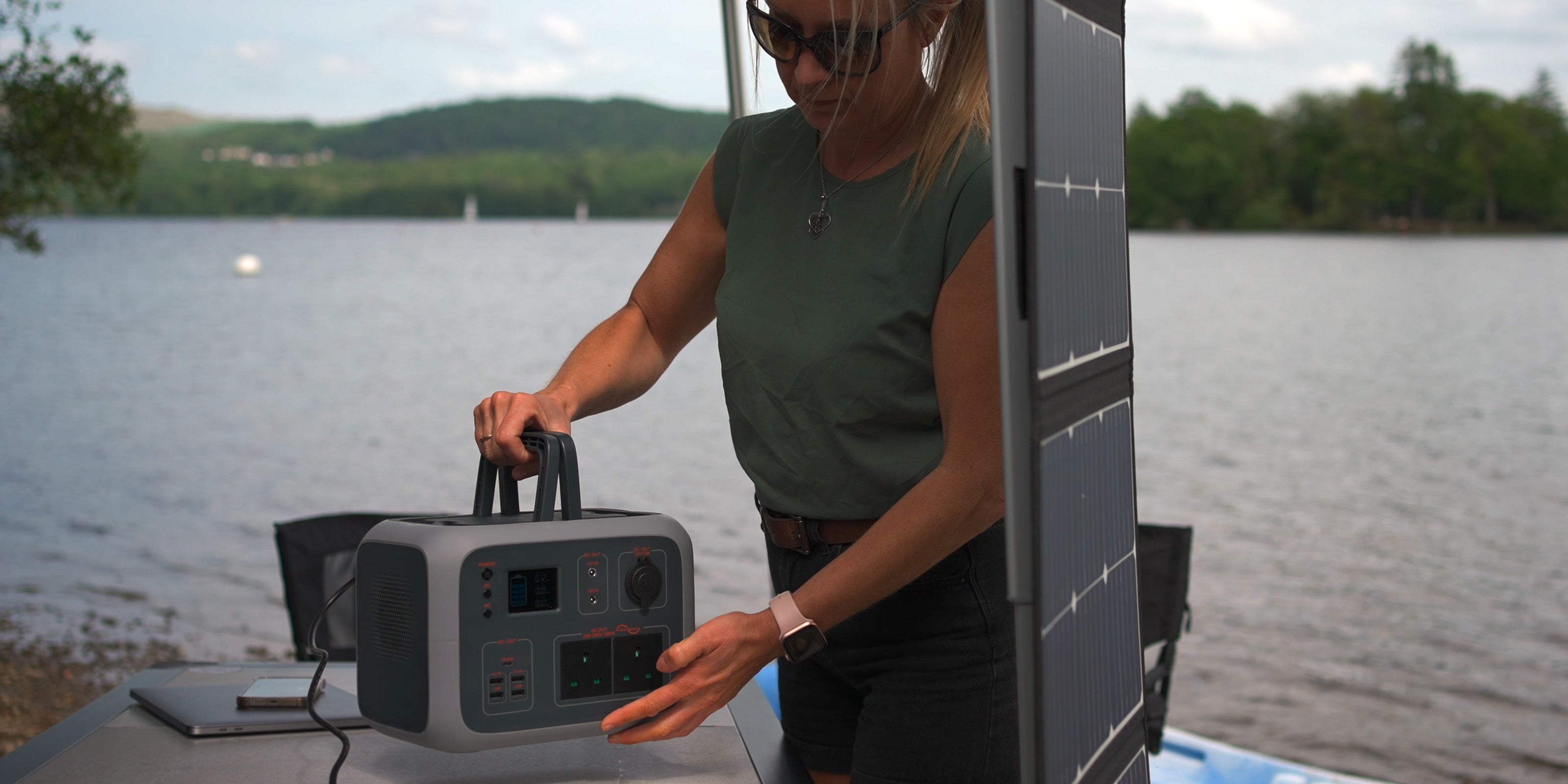 Image of a woman holding a TP500 power station by its handles to be placed on a table next to a TS100 solar panel